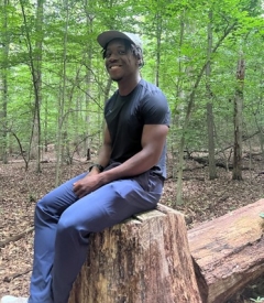 Dami smiling while sitting on a tree stump in the woods